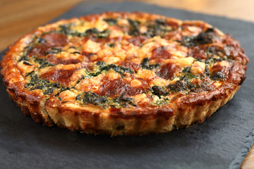Italian traditional rustic quiche pizza with cheese, spinach  and tomatoes on a black plate in restaurant