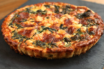 Italian traditional rustic quiche pizza with cheese, spinach  and tomatoes on a black plate in restaurante