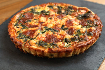 Italian traditional rustic quiche pizza with cheese, spinach  and tomatoes on a black slate plate in restaurant