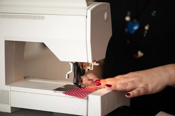 detail of womans hands sewing maching Seamstress sews clothes made of red cloth on a sewing...