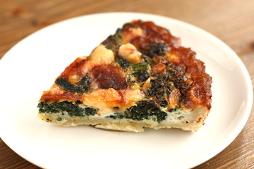 Fench traditional rustic slice of quiche pizza with cheese, spinach  and tomatoes on a black slate plate in restaurant