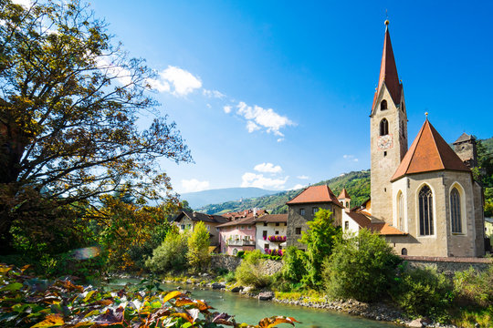 church and colorful houses along river Isarco, Chiusa, Italy