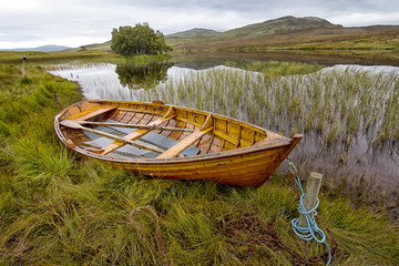 Landschaft in Schottland mit Holzboot am Ufer eines Sees