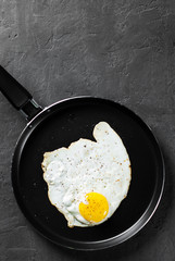 Fried egg in a iron frying pan on Dark grey black slate background