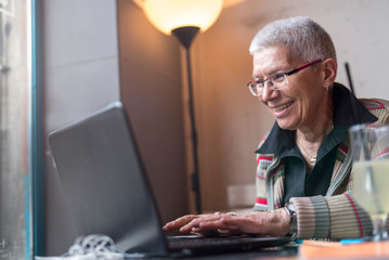 Happy senior old woman sitting in a coffee shop and doing some work on her laptop or browsing the internet