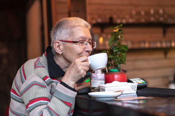 Senior old woman enjoying her aromatic coffee in a modern cafe