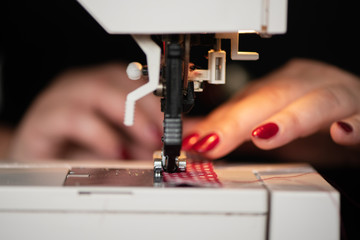 detail of womans hands sewing maching Seamstress sews clothes made of red cloth on a sewing machine. Work by the light of the built-in hardware lamp. Steel needle with looper and presser foot close-up