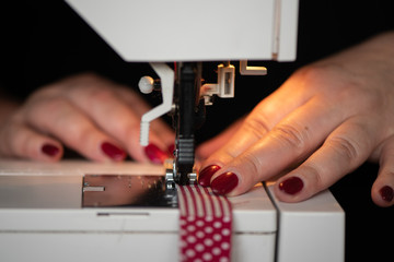 detail of womans hands sewing maching Seamstress sews clothes made of red cloth on a sewing machine. Work by the light of the built-in hardware lamp. Steel needle with looper and presser foot close-up