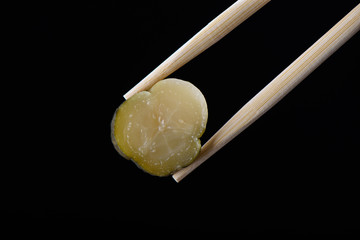 Chopsticks with a slice of pickled cucumber isolated on a black background