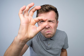Young caucasian man gesturing with hand showing small size sign with fingers.
