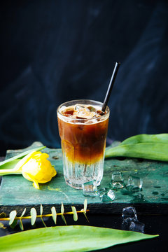 Vertical image of iced drink on top of soda on black background. Yellow tulips on the table.