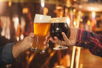 Cropped close up of two men clinking beer glasses together, celebrating at the beer pub....