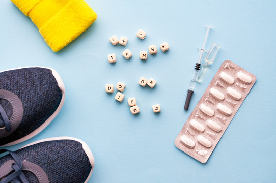 The concept of doping in sport. Inscription vitamins or doping on a blue background. Sports shoes, pills, syringe with medicine, wrist support.