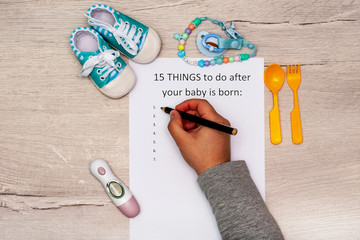 Caption: 15 things to do after your baby is born. A4 sheet on a wooden background next to children's things.