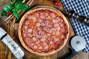 Top view on homemade italian pizza with pepperoni. Pizza on rustic wooden background with tomato, salami, basilic. Copy space. Traditional italian cuisine. Flat lay picture for recipe or menu