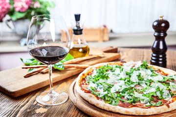 Close up view on traditional italian lunch. Pizza with prosciutto and red wine glass on rustic wooden table. Copy space for design. italian cuisine. Flat lay picture for recipe or menu