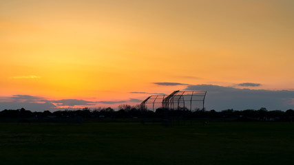 A basebll backstop on a practice field in the evening.