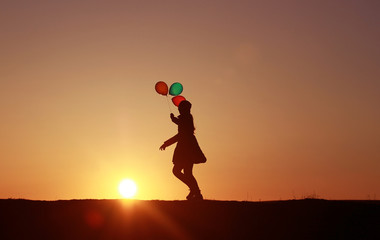Girl runs with balloons on the background of the sunset to the sun
