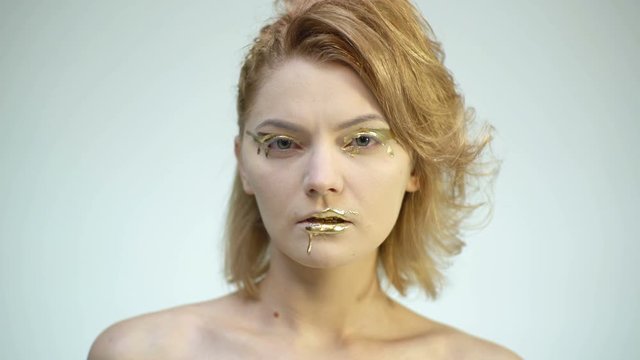 Gold Paint drips from the lips, lipgloss dripping from sexy lips, golden liquid drops on beautiful model girl's mouth, gold metallic skin make-up. Beauty woman face makeup close up.
