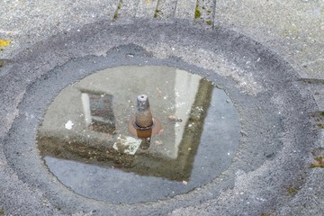 Spiegelung eines Gebäudes in der Wasserpfütze eines Wasserspenders, Deutschland