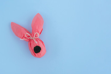 Easter bunny gift egg wrapped in coral craft paper on blue background.