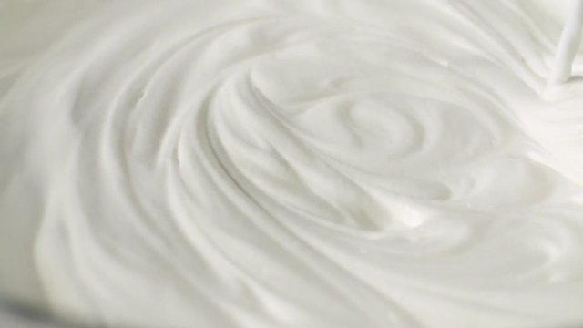 Whipping white cream with a mixer in slow motion side view