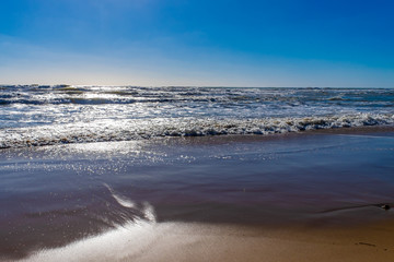 Colorful sunset at the tropical sandy beach, waves with foam hitting sand