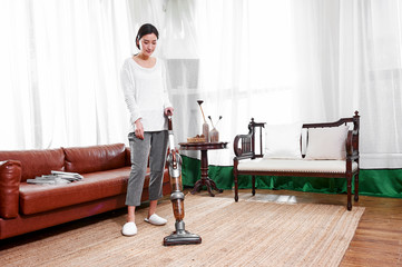 Asian teenage girl using a wireless vacuum cleaner to clean the carpet in the living room in the...