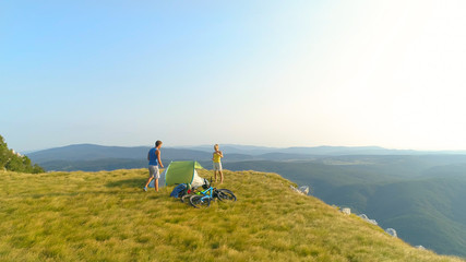 AERIAL: Flying over mountain biking couple preparing a tent in the mountains.