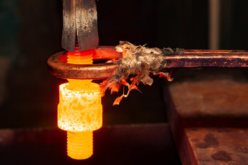 closeup calcining hot metal steel gear parts in a factory induction furnace with smoke