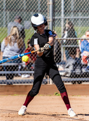 Female softball player in black uniform making contact with bat on pitched ball during game.