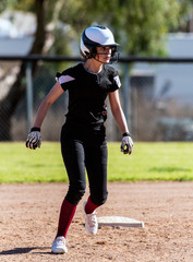 Female softball player in black uniform taking an agressive lead off second base and remaining...