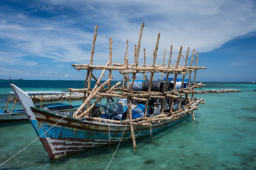Abandoned fishing boat in the harbor of Harapan Island with an unique wooden design and barrel above it