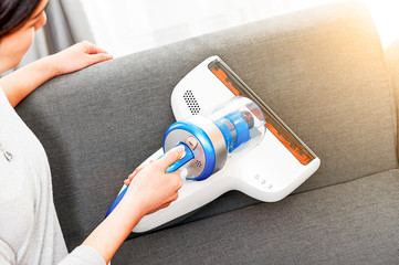 Asian girl uses a vacuum cleaner to vacuum the dust on the sofa