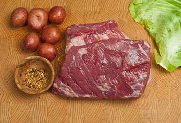 Top view, medium distance, three pound, raw, corn beef brisket, six small, red, potatoes, rare, bowl of dill, leaf of cabbage, bamboo, wood, cutting board ingredients for, St patrick's day dinner