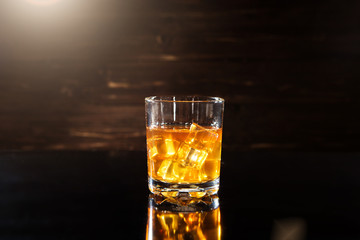 Glass of whiskey with ice cubes on black table
