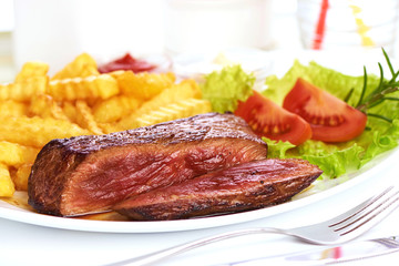 Grilled medium rare beef steak with french fries, sliced fried meat, close-up