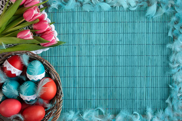Wielkanocne tło -  kolorowe pisanki w koszyku i rożowe tulipany na niebieskiem tle