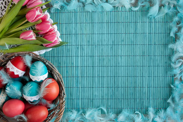 Kolorowe pisanki w koszyku i rożowe tulipany na niebieskiem tle