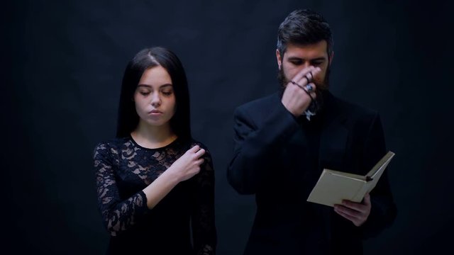 Girl and priest dressed in black baptized on a black background. Priest prays on a black background. Religious nun in religion concept against dark background. religion opium for the people.