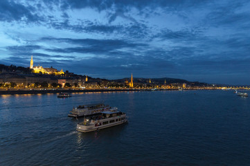 Fototapeta premium Two ships move away on the Danube as it passes through Budapest with Fishermen's Bastion and the illuminated Buda shore, Hungary
