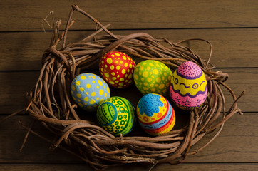 Colorful decorated easter eggs on a nest made of branches against wooden background