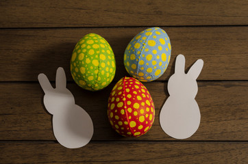 Colorful decorated easter eggs and white paper bunnies on wooden background