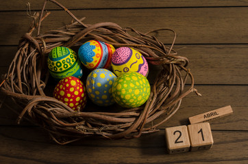 Colorful decorated easter eggs on a nest made of branches and March 21 date on cube wooden calendar against wooden background