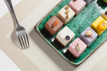 Dessert. Assorted fruit pastries made from natural products on a beautiful, green plate on a beige napkin on the background. Nearby is a fork. Cakes with fresh berries and nuts.