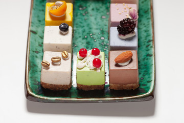 Dessert.  Assorted fruit pastries made from natural products on a beautiful, green plate on a white background. Cakes with fresh berries and nuts.