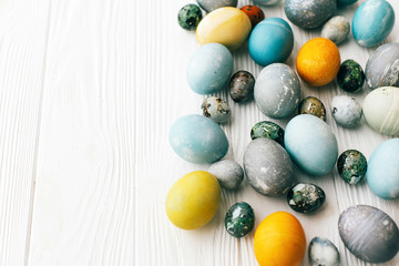 Stylish Easter eggs border on white wooden background, copy space. Modern easter eggs painted with natural dye in yellow,blue,green,grey colors. Happy Easter greeting card