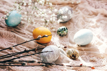 Stylish Easter eggs with spring flowers and willow branches on rustic fabric in sunny light on wood. Modern colorful eggs painted with natural dye. Happy Easter, seasons greetings