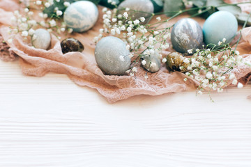 Happy Easter. Stylish Easter eggs on rustic fabric with spring flowers and eucalyptus branch on white wooden background. Modern pastel eggs painted with natural dye. Greeting card