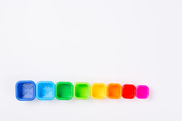 Pyramid line tower build from colored plastic tubs cups placed on white background desk. Toy for babies and toddlers to joyfully learn mechanical skills and colors. Baby development. Flatlay. Space